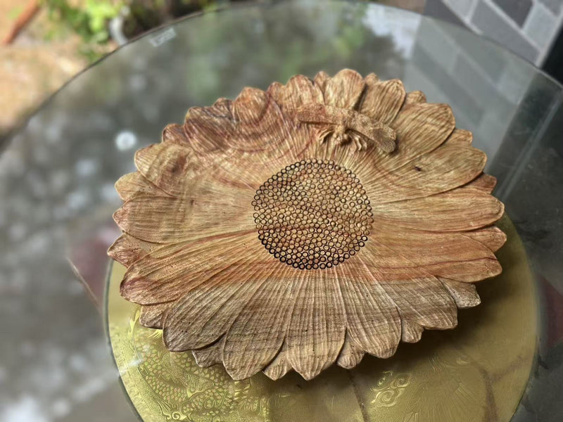 A flower-shaped wooden tray with a textured centre resting on a glass table.