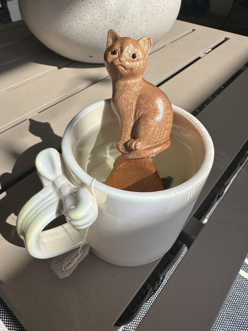 A wooden spoon with a carved cat handle standing in a pale cup in sunlight.