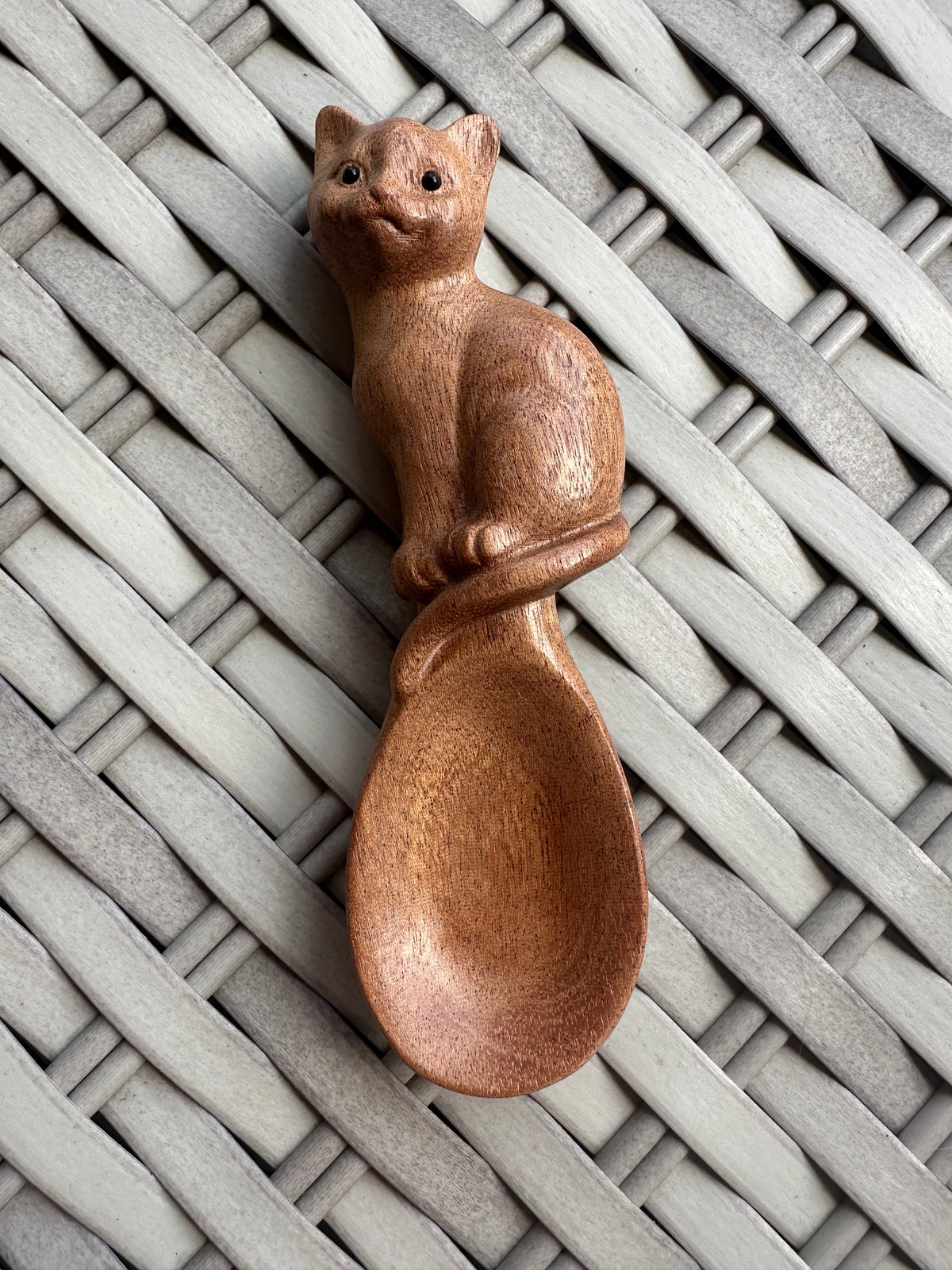 Wooden spoon with a carved cat-shaped handle resting on a pale woven surface.