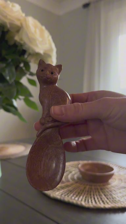 Silent close-up: a hand holds the cat-shaped wooden spoon, followed by a closer view of its carved face and bowl.