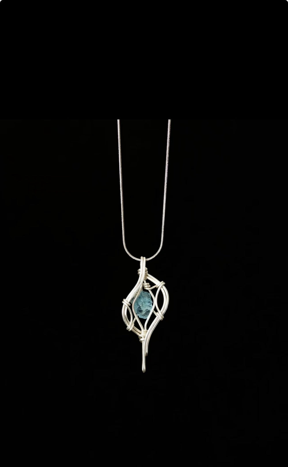 Blue pendant enclosed in flowing silver-toned wire on a chain against black.