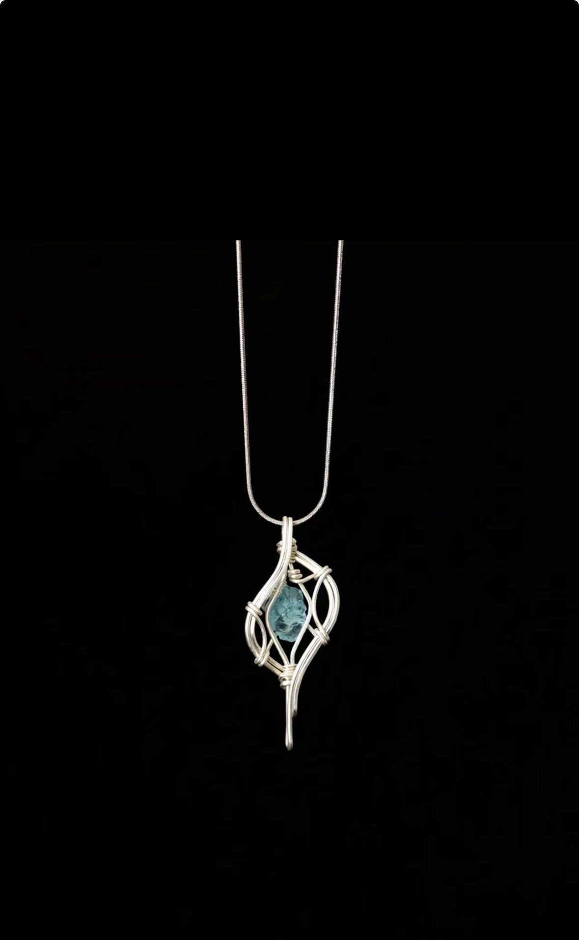 A textured blue pendant enclosed in flowing silver-toned wire, hanging on a chain against black.