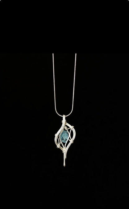 A textured blue pendant enclosed in flowing silver-toned wire, hanging on a chain against black.