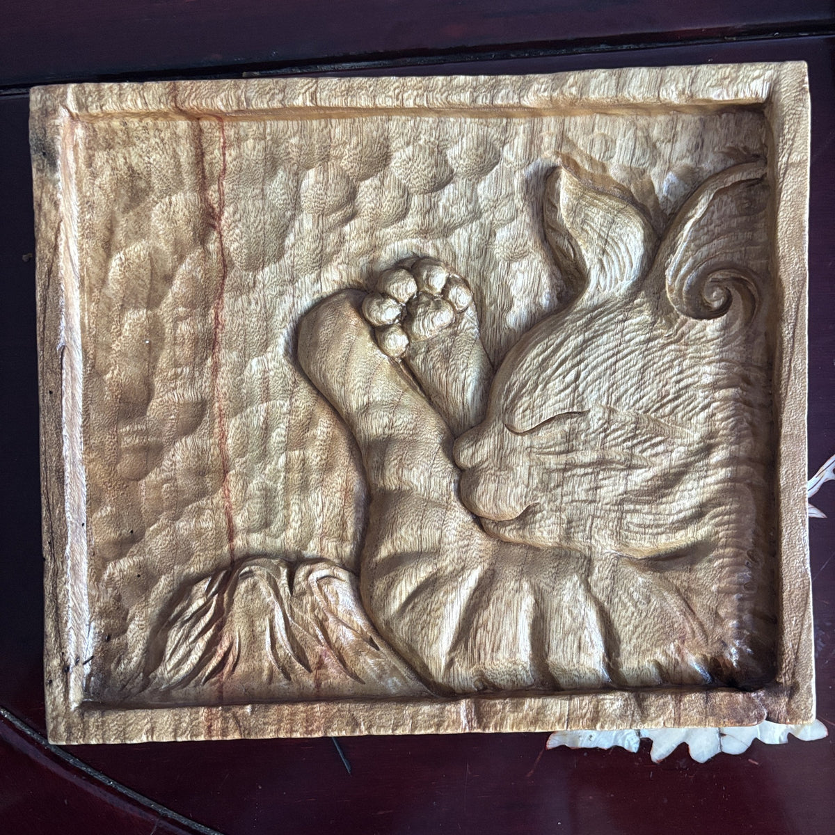 A square wooden tray with a carved resting cat, raised paw and textured border.
