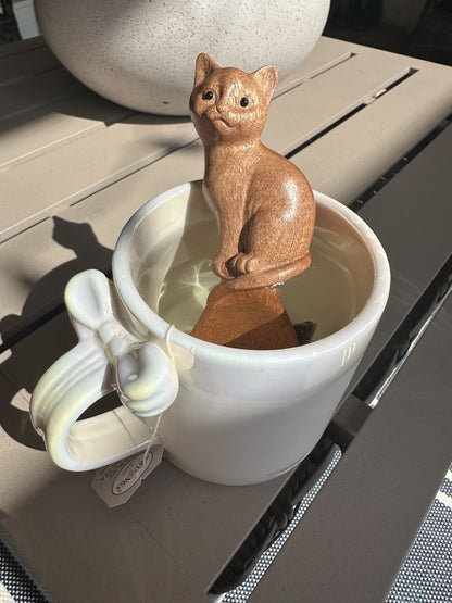 A wooden spoon with a carved cat handle standing in a pale cup in sunlight.